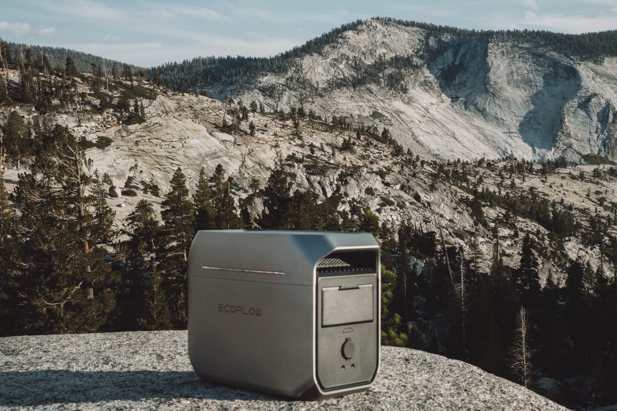 The DELTA 3 Plus from its rear corner on a granite slab, back-panel cover closed, a granite ridge and pines behind