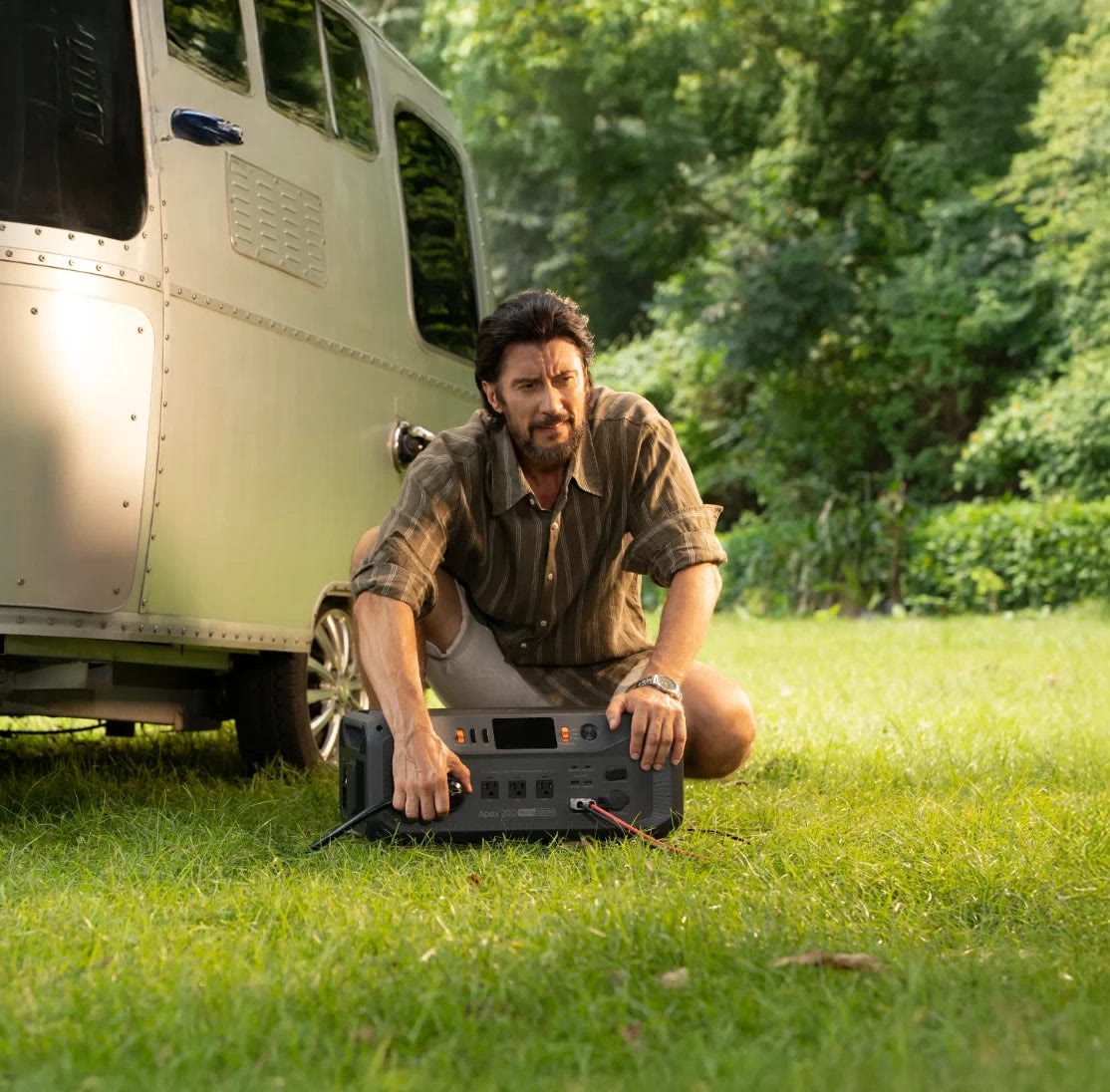 BLUETTI image of a man setting the Apex 200 down on grass beside a travel trailer